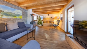 Ein gemütliches Wohnzimmer mit Steinwand, Kamin, einer Couch, einem Weihnachtsbaum und einem großen Fenster.