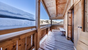 Eine Holzdielen-Terrasse mit einer Bank, mit Blick auf eine verschneite Berglandschaft.