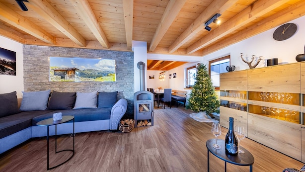 Ein gemütlicher Wohnraum mit Steinwand, Holzbalkendecke, Kamin und Weinkühlschrank, dazu ein Weihnachtsbaum.