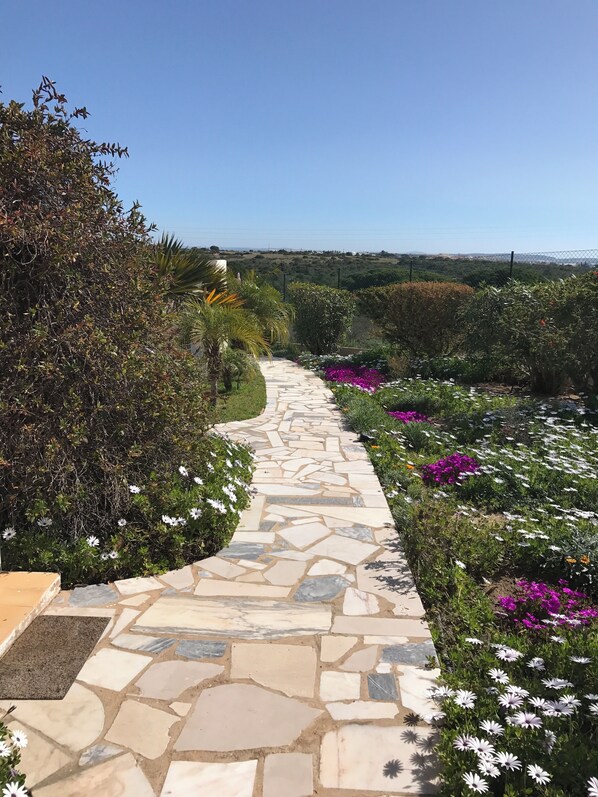 A stone pathway leading through a garden with various plants and flowers. - Detached villa with sea view, heated pool and air conditioning (Caramujeira)
