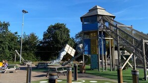 Une aire de jeux avec une structure d’escalade, des balançoires et un toboggan.