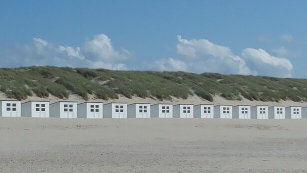 Une rangée de cabanes de plage, avec un ciel dégagé et des dunes en arrière-plan.