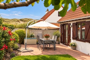 A patio with a table and chairs, a white umbrella, and a garden with red flowers.