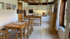 A kitchen with wooden cabinets, a dining table, and chairs. There is a window with curtains. - Directly behind the dunes in the Fabiola Beach Park (Wenduine)