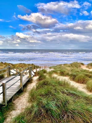 A wooden boardwalk leading to a beach with dunes and a view of the ocean.