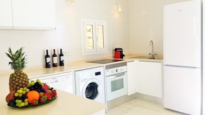 Una cocina moderna con muebles blancos, lavadora integrada, estufa y refrigerador.