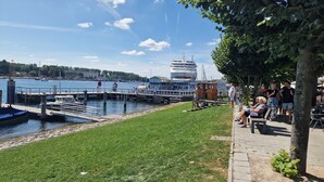 Ein Yachthafen mit vertäuten Booten, eine Pier mit Spaziergängern und eine Rasenfläche mit Bänken.