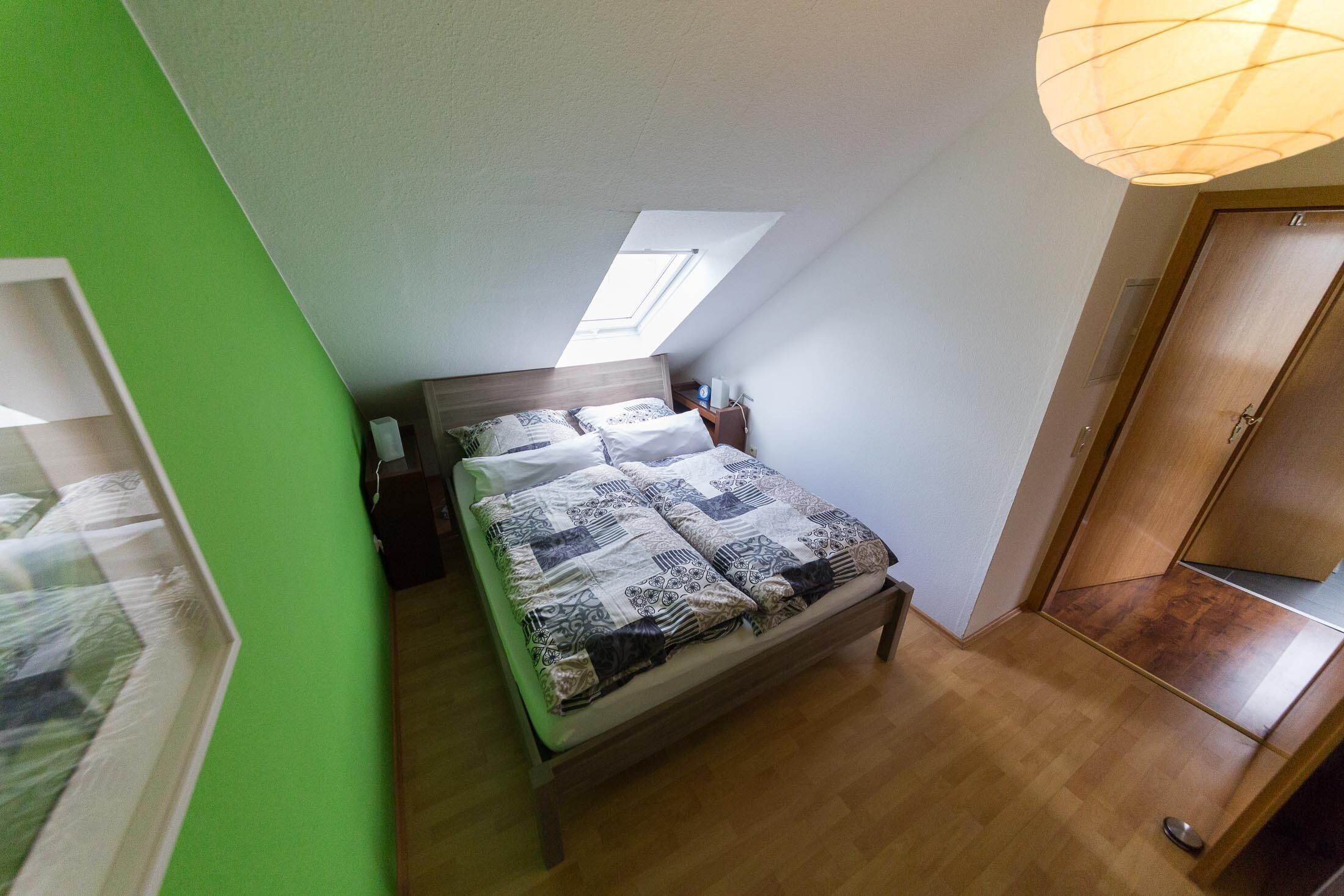 Une chambre avec un plafond en pente, un lit avec une literie à motifs, une table de chevet et une armoire en bois.