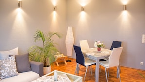 A modern living room with a dining area, featuring a sofa, chairs, a table, and a potted plant. - Relaxation in the vineyards - Ferienwohnung Isinger (Rüdesheim am Rhein)