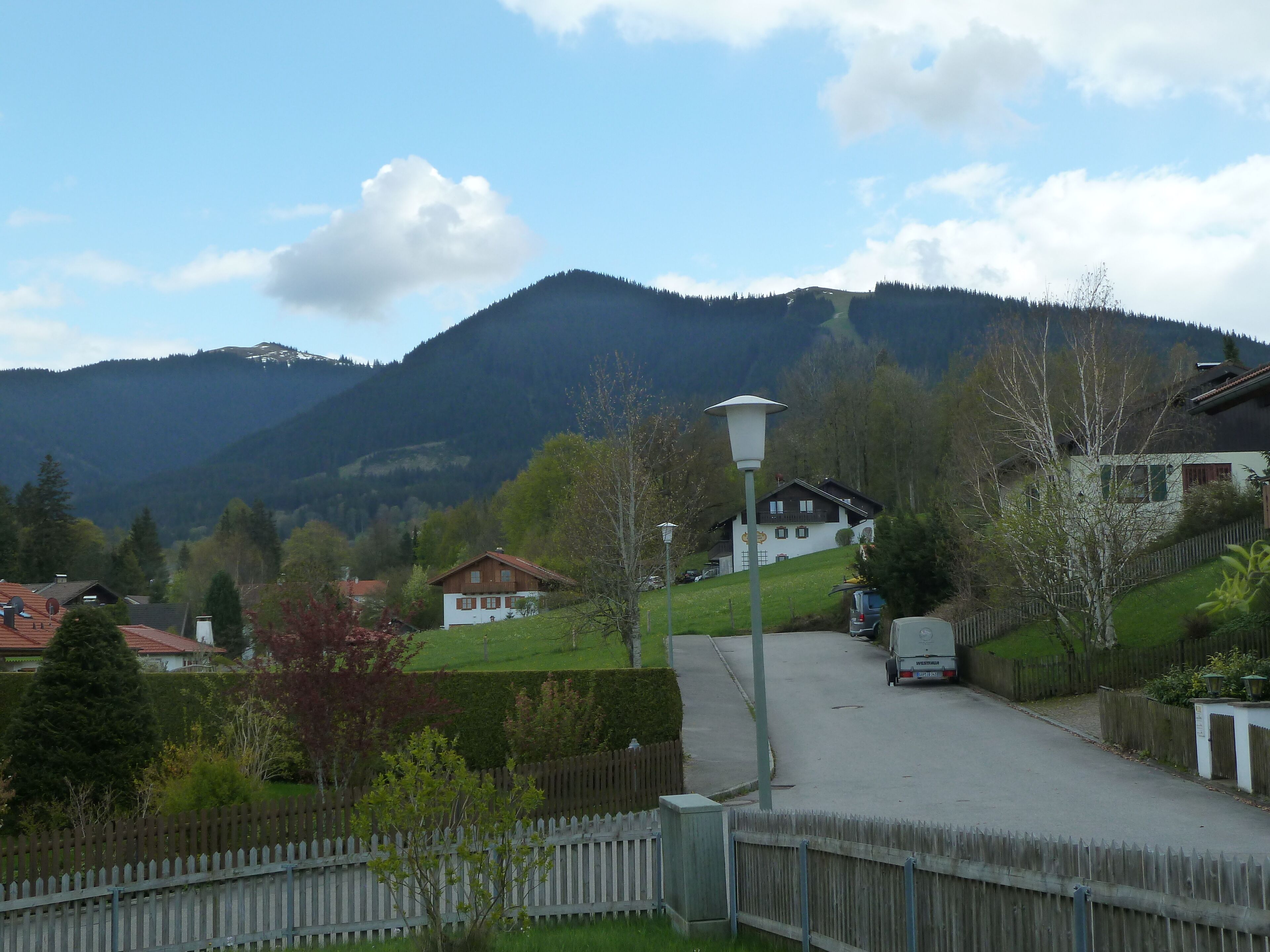 Une rue de campagne bordée de maisons, avec un lampadaire et une montagne en arrière-plan.