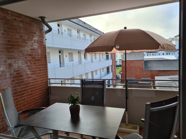 A balcony with a table, chairs, a potted plant, and a large umbrella.