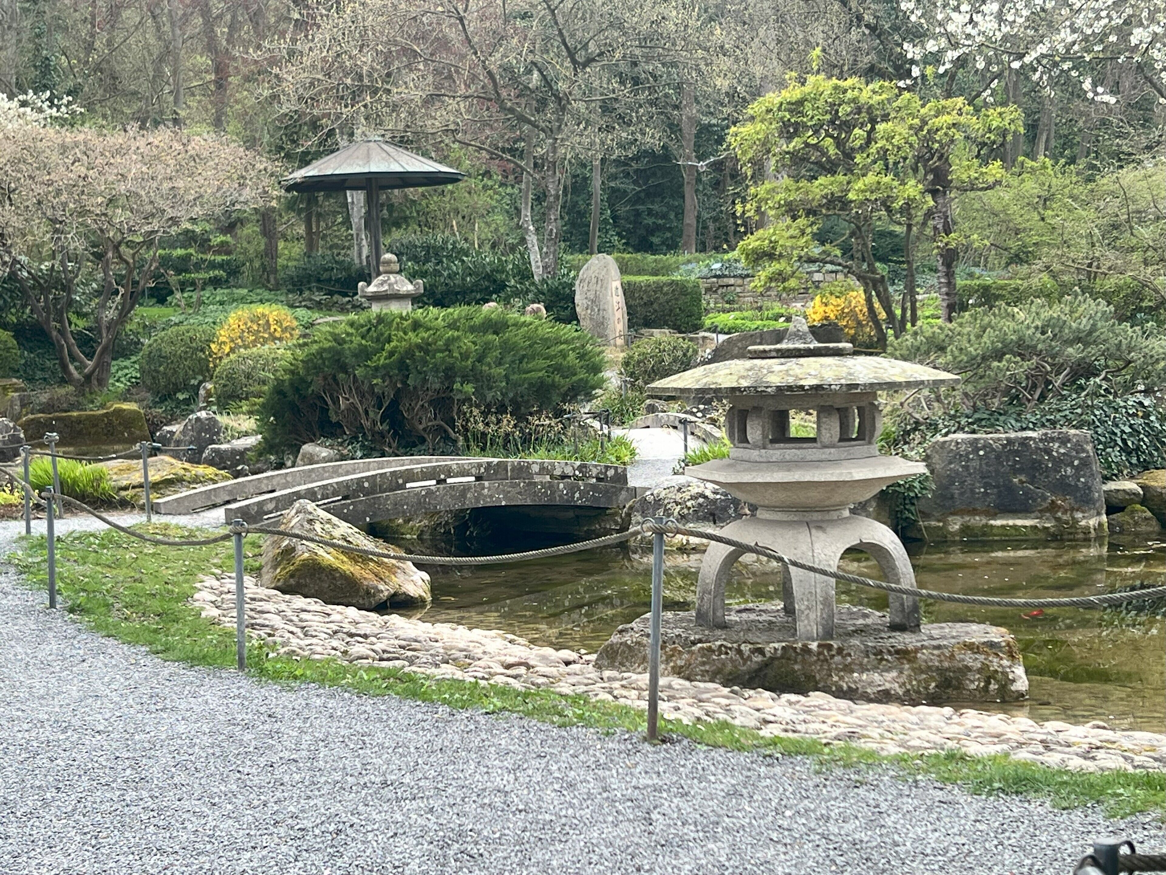 Un jardín japonés tradicional con un farol de piedra, un pequeño puente y una pagoda de piedra.