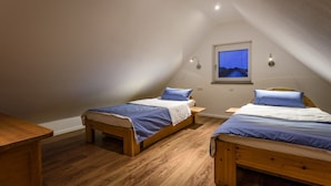 Un dormitorio ático pequeño y acogedor con dos camas de madera, un ventanal con vistas y una mesa de madera.