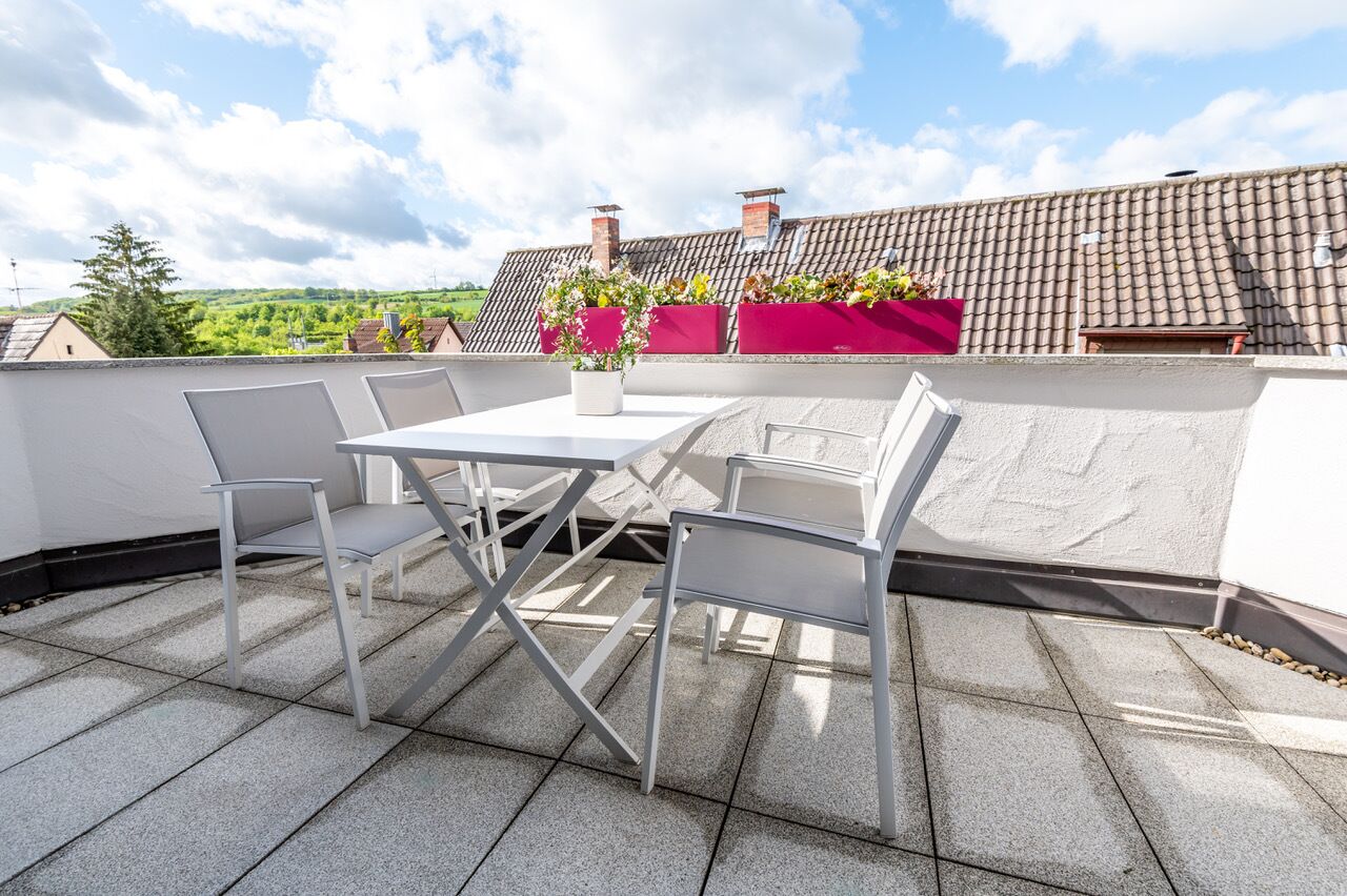 Eine Dachterrasse mit Tisch und Stühlen, Blumentöpfen und Blick auf die umliegende Landschaft.