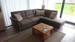 A modern living room with a brown sectional sofa, a wooden coffee table, and a view of a green garden through large windows.