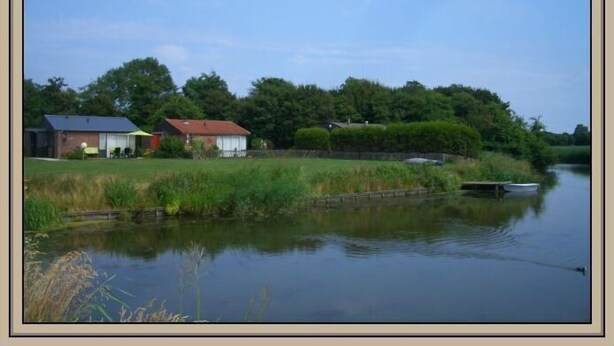 A calm river with a small boat, houses along the riverbank, and lush greenery.