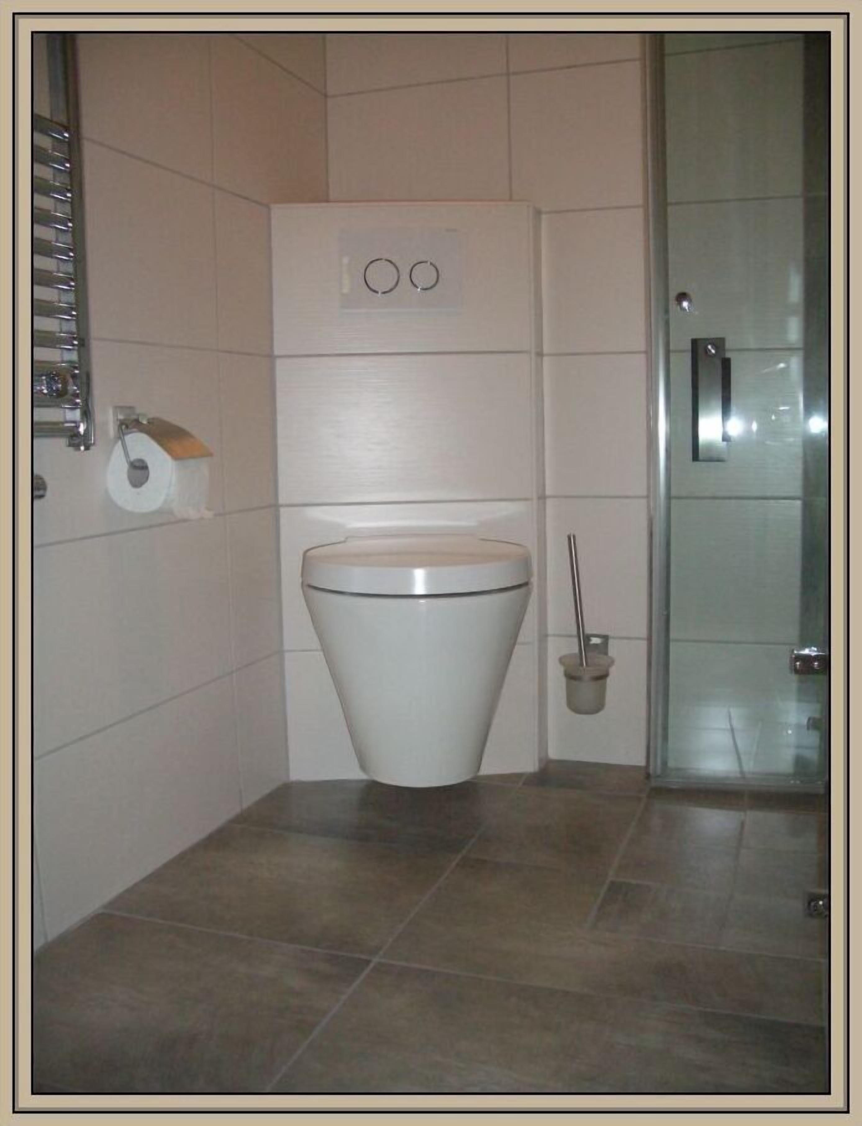 A modern bathroom with a white toilet, a hand dryer, and a glass shower enclosure.