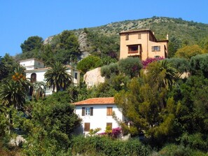 Une propriété située sur une colline, comprenant plusieurs bâtiments, notamment une maison blanche avec un toit rouge et un bâtiment brun doté d’un balcon.