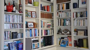 Una estantería bien organizada con libros, adornos y algunas fotografías enmarcadas.