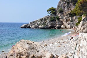 Une plage de galets avec une eau cristalline, un escalier en pierre et des gens qui prennent un bain de soleil.