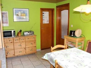 Ein Zimmer mit Bett, Holzkommode, Mikrowelle, Radio und einer Tür mit einem Poster.
