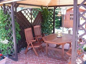 Eine Hollaube mit Tisch und Stühlen, umgeben von Grünpflanzen.