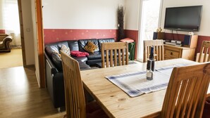 A living room with a wooden dining table, a black leather sofa, and a television mounted on the wall. - Apartment Casa Casimir with Elbe view balcony & large garden (for soccer/volleyball) (Dresden)