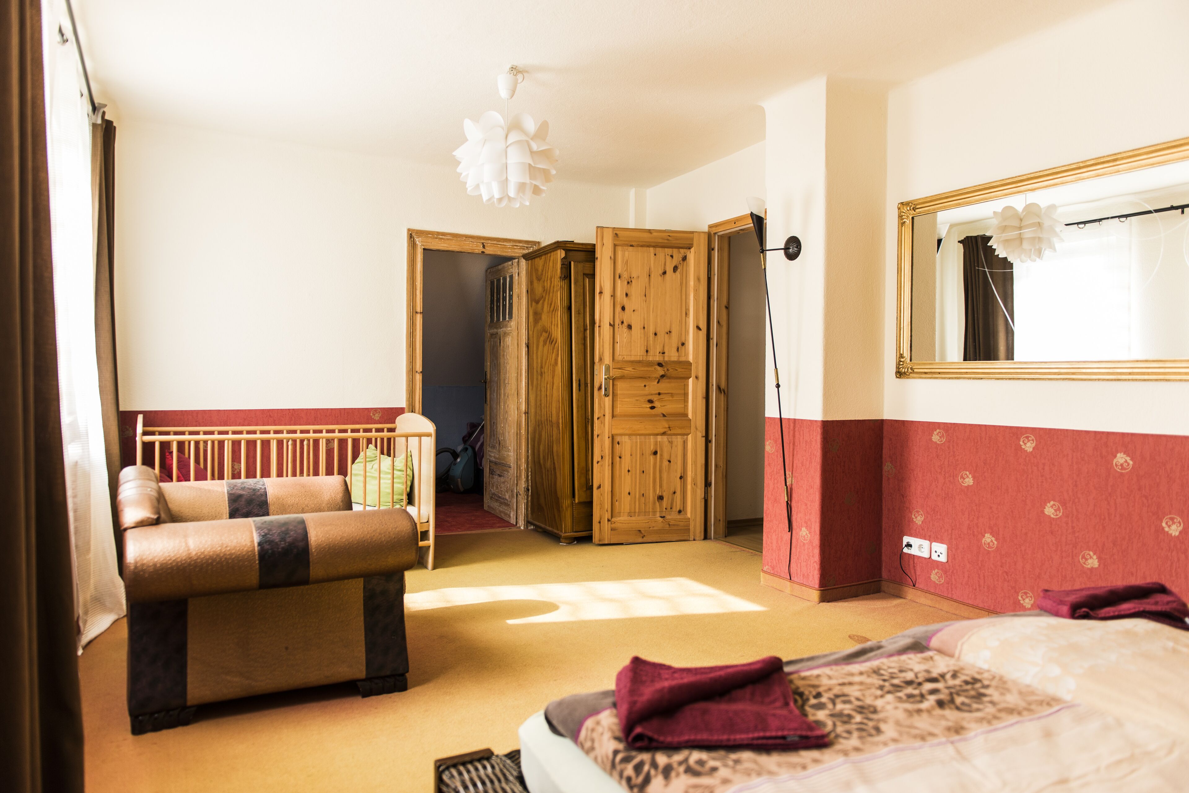 Ein Schlafzimmer mit Bett, Sofa, einem Holzschrank und einem Spiegel.