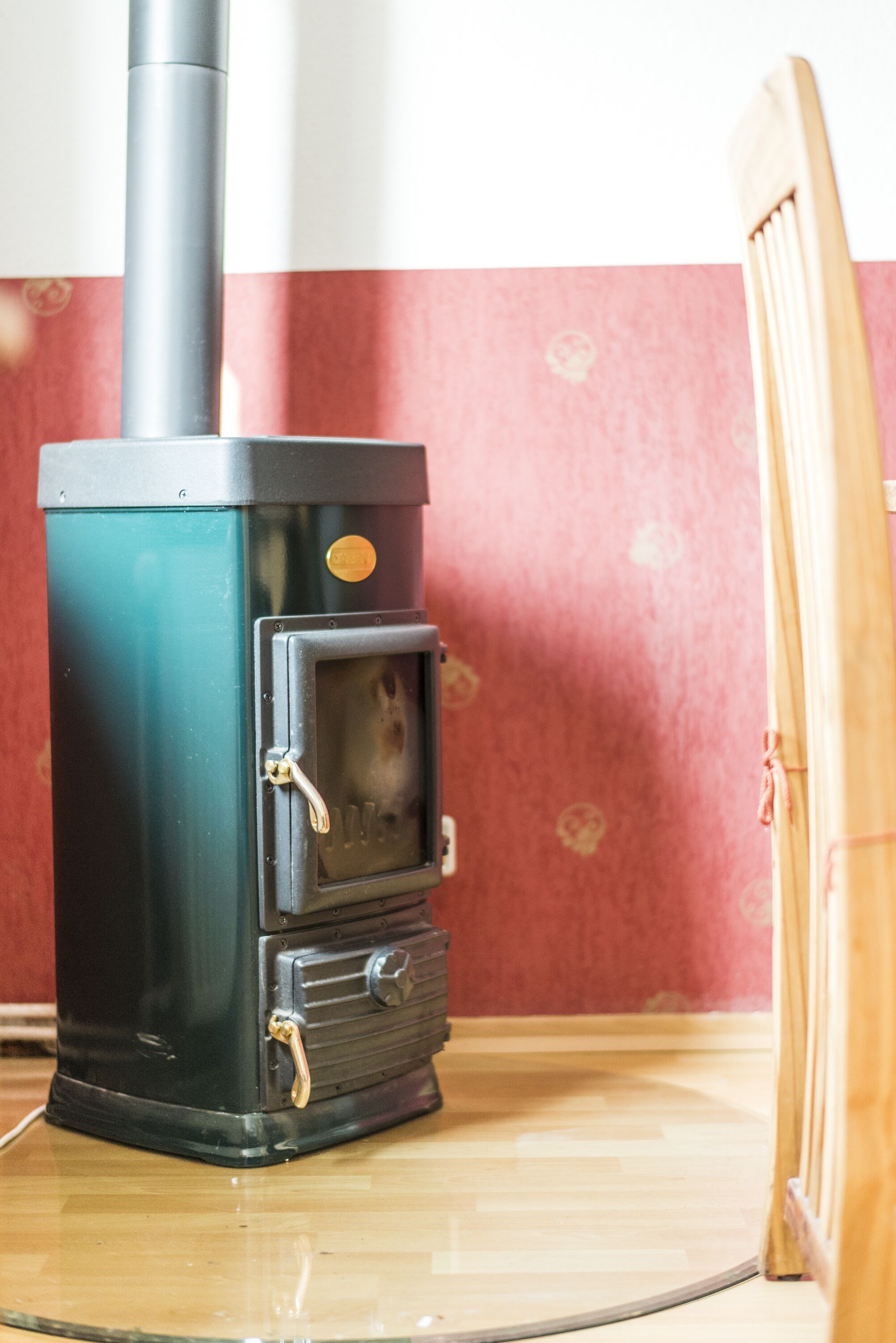 Una estufa de leña con chimenea, un ventanal pequeño y una puerta con picaporte.