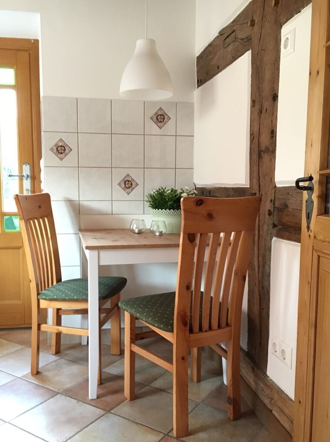 Een keuken met twee houten stoelen, een witte hanglamp en een betegelde achterwand.