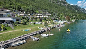 A lakeside resort with villas, a dock with boats, and a mountainous backdrop.