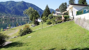 A lakeside property with a grassy slope, a white building with a green fence, and mountains in the background.