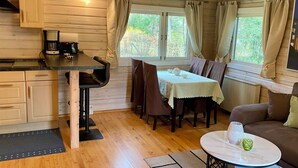 Een gezellig interieur van een chalet met een eettafel, stoelen, een bank, een koffiezetapparaat en een raam met gordijnen.