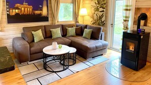 Een gezellige woonkamer met een hoekbank, een ronde salontafel, een open haard en een groot raam met gordijnen.