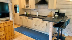 Een moderne keuken met houten kastjes, een inbouwoven, een koffiezetapparaat en een barstoel.