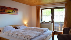 A room with a wooden bed, a painting of a sunset scene, a window with curtains, and a chair. - Apartment with panoramic views (Halblech)