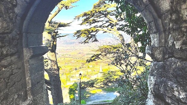 A stone archway leading to a pathway surrounded by greenery and a view of a valley.