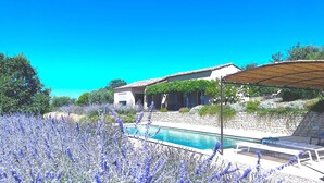 A pool area with a stone wall, a covered seating area, and a building with a tiled roof.