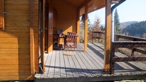 Een houten hut met een terras, een tafel en stoelen.