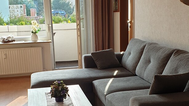 Een moderne woonkamer met een grijze modulaire bank, een houten salontafel en uitzicht door een glazen deur op het buitengebied.