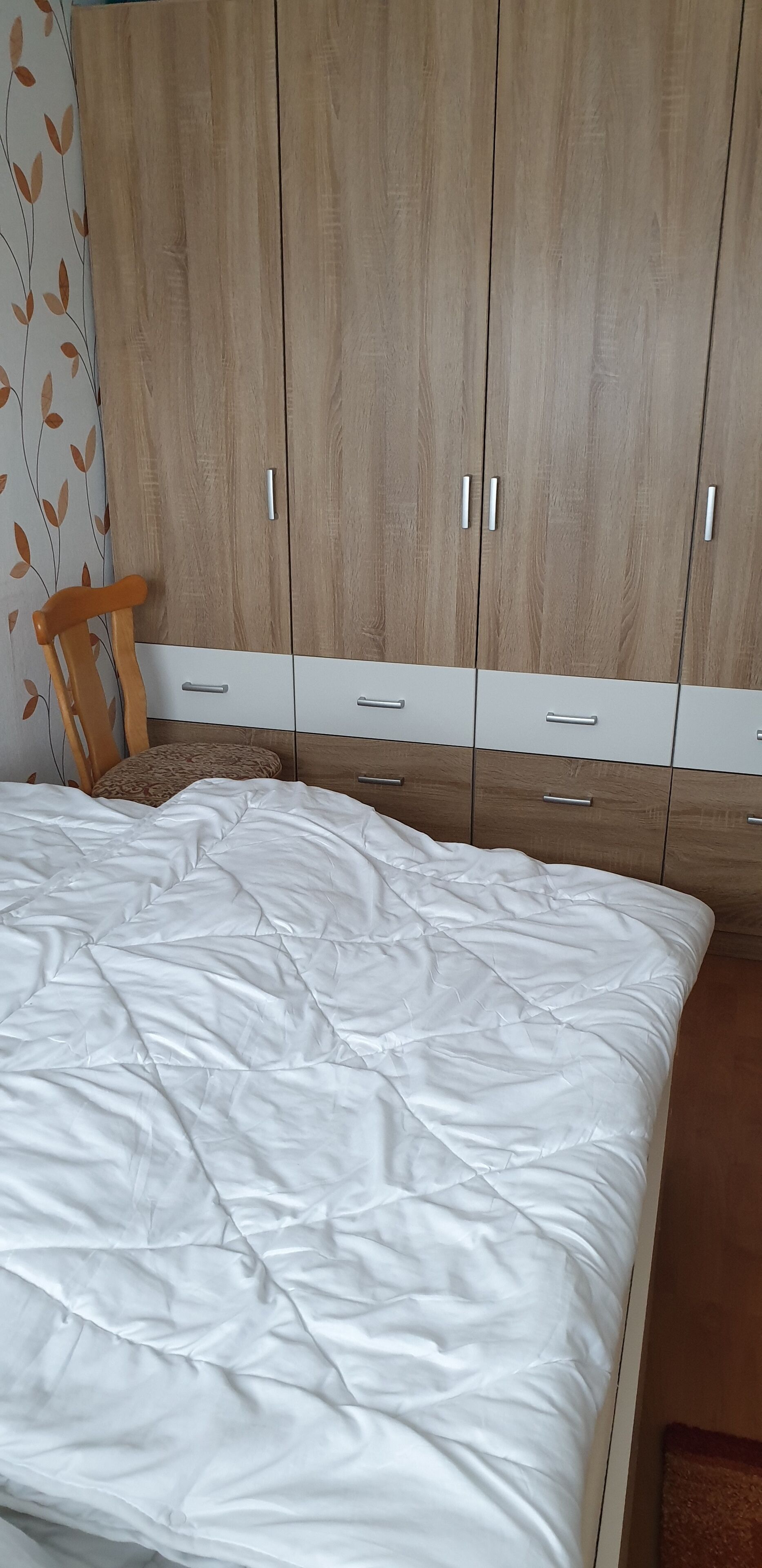 A bedroom with a bed, wooden wardrobe, and a chair.