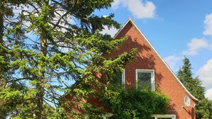 A red brick house with a sloped roof, a small porch with a chair, and a large tree in front. - To get my head clear! Cozy cottage in Ditzum, large garden, dogs ok! (Ditzum)