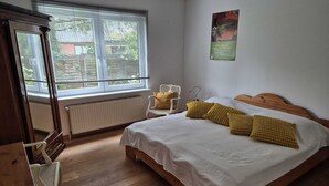A bedroom with a wooden bed, white bedding, a chair, a radiator, and a window with blinds. - To get my head clear! Cozy cottage in Ditzum, large garden, dogs ok! (Ditzum)
