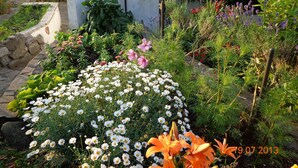 Un jardin agrémenté de diverses fleurs et plantes, un sentier en pierre et un bâtiment doté d’un toit en tuiles.