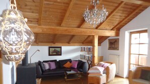 Un salon spacieux avec un plafond en bois, une cheminée, un ensemble de canapés, une bibliothèque et une grande fenêtre.