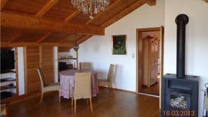 Un intérieur en bois comprenant une table à manger, des chaises, un lustre, un tableau et un poêle à bois.
