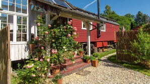 A red wooden house with a porch, potted plants, and a gravel path.