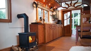 A cozy kitchen with a wood-burning stove, wooden cabinets, and a large window.