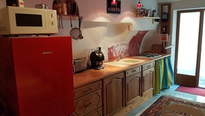 Une cuisine de taille réduite, avec un réfrigérateur rouge, un four à micro-ondes, un grille-pain et un évier. Une fenêtre offre une vue sur l’extérieur.