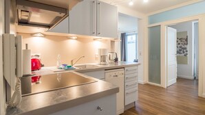A modern kitchen with a stainless steel sink, a red kettle, and a coffee maker. There is a window with curtains and a door leading to another room. - App. 02 / EC - Apartment No. 02 in the sunbath (Sassnitz)